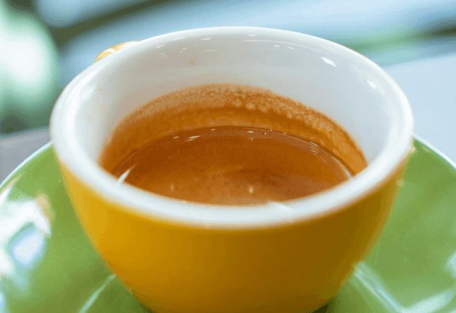 Espresso servito in una tazzina gialla su piattino verde presso CoffeeStorming.