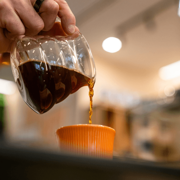 Versamento di caffè filtrato in una tazzina arancione, catturando l'essenza della qualità di CoffeeStorming.